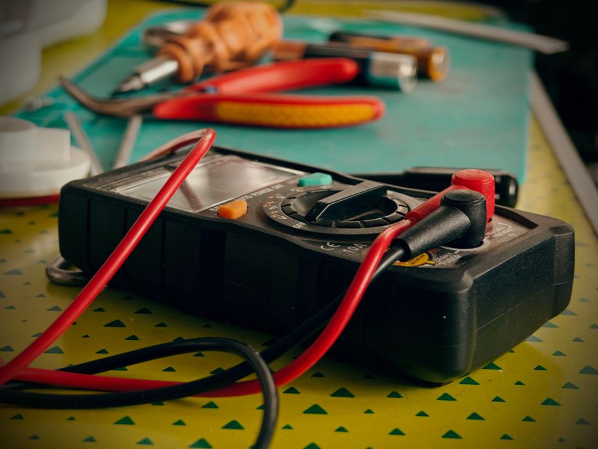 Close-up view of a multimeter and various tools on a workspace table.