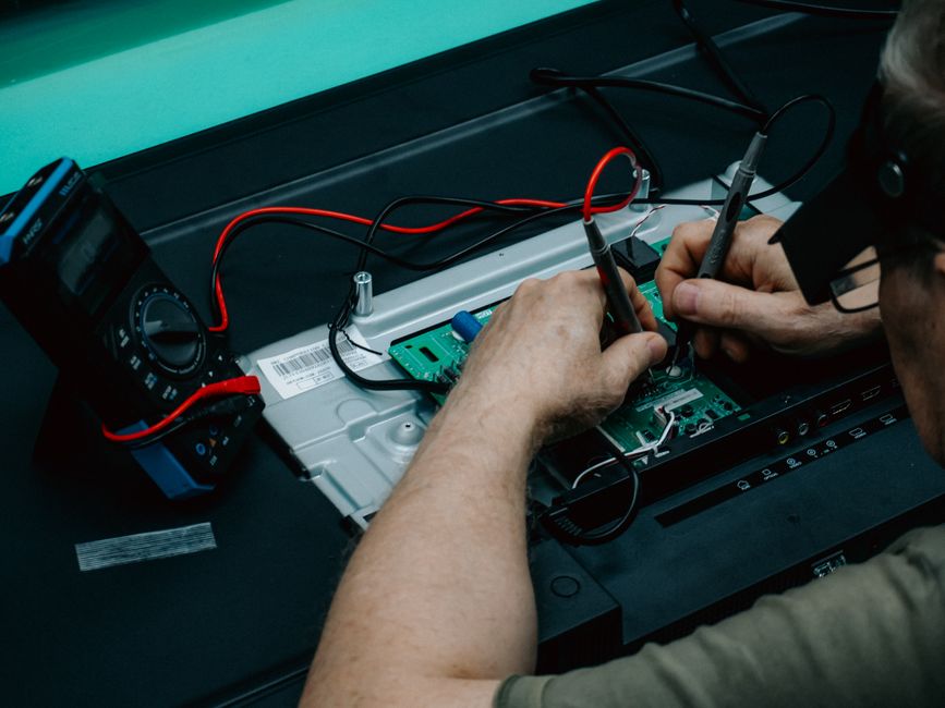 A technician uses a multimeter to repair a circuit board, focusing on precision electronics work.